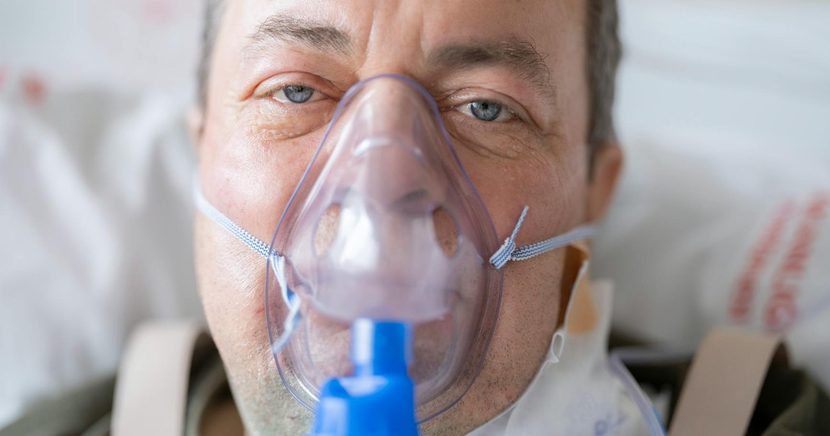 Close-up of a man in a hospital bed wearing an oxygen mask, highlighting healthcare needs.