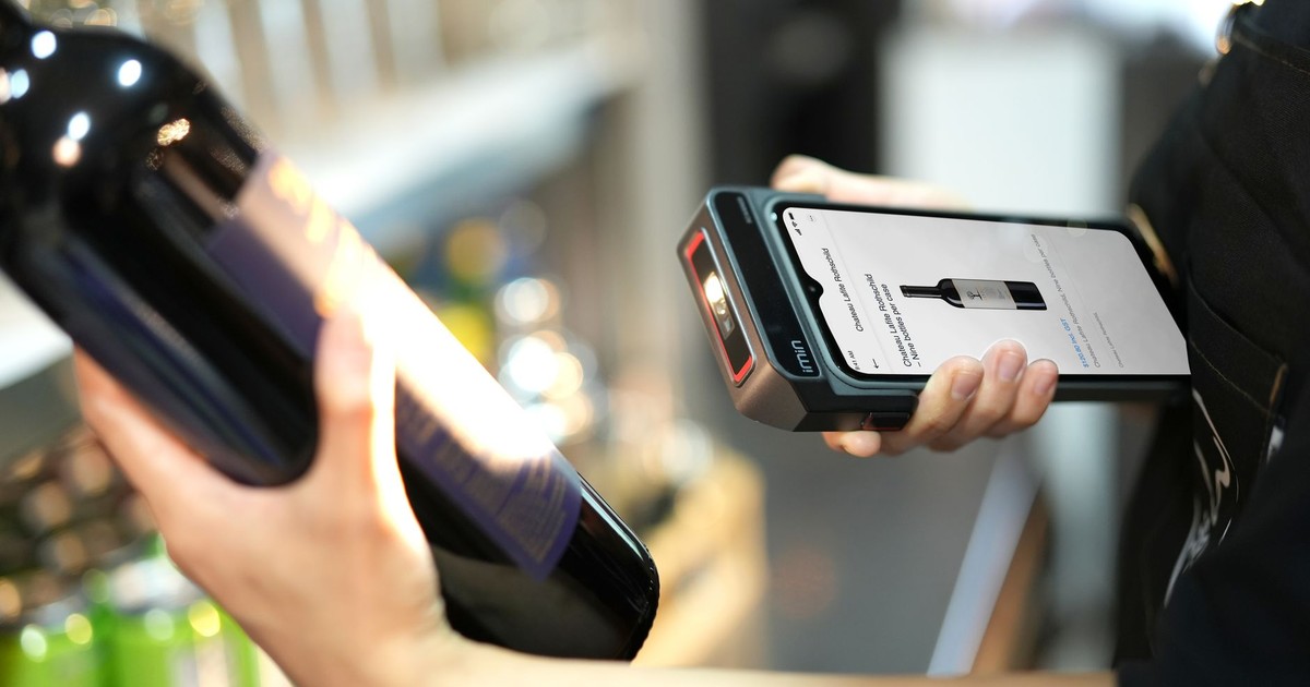 Close-up of a person scanning a wine bottle with a portable scanner in a store.
