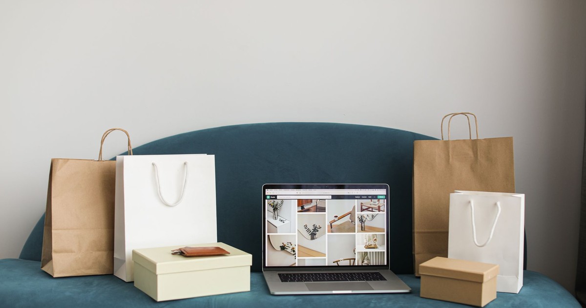 A laptop surrounded by shopping bags and boxes on a blue sofa, ideal for online shopping themes.