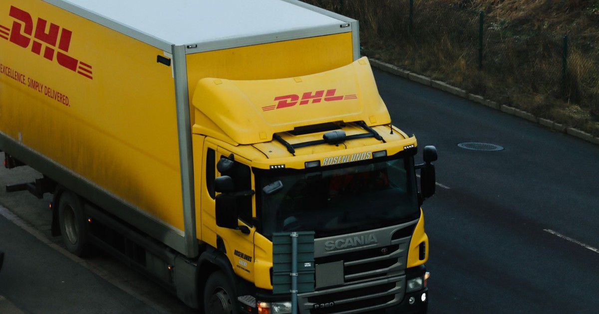 Yellow DHL delivery truck driving along a city road showcasing logistics in action.
