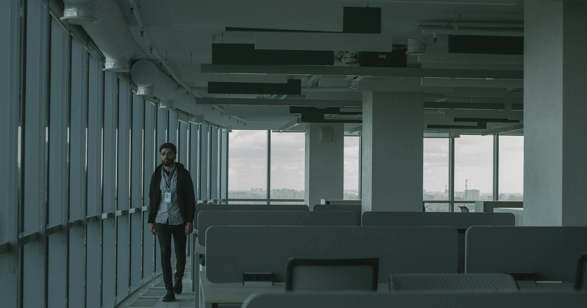 A dimly lit empty office space with one person walking, providing an atmosphere of isolation.