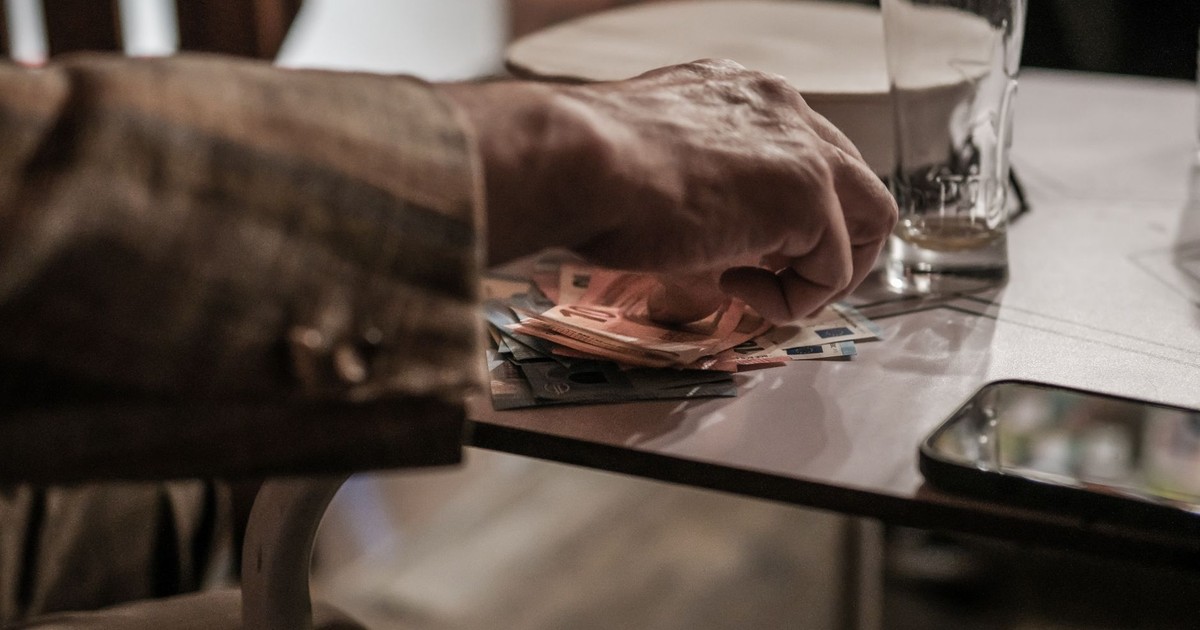 Hand counting euro banknotes on a table beside a phone and empty glass.