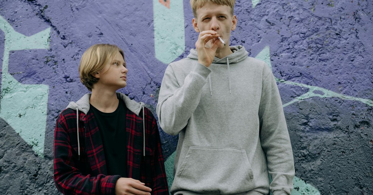 Two teenagers standing by a graffiti-covered wall, one smoking a cigarette.