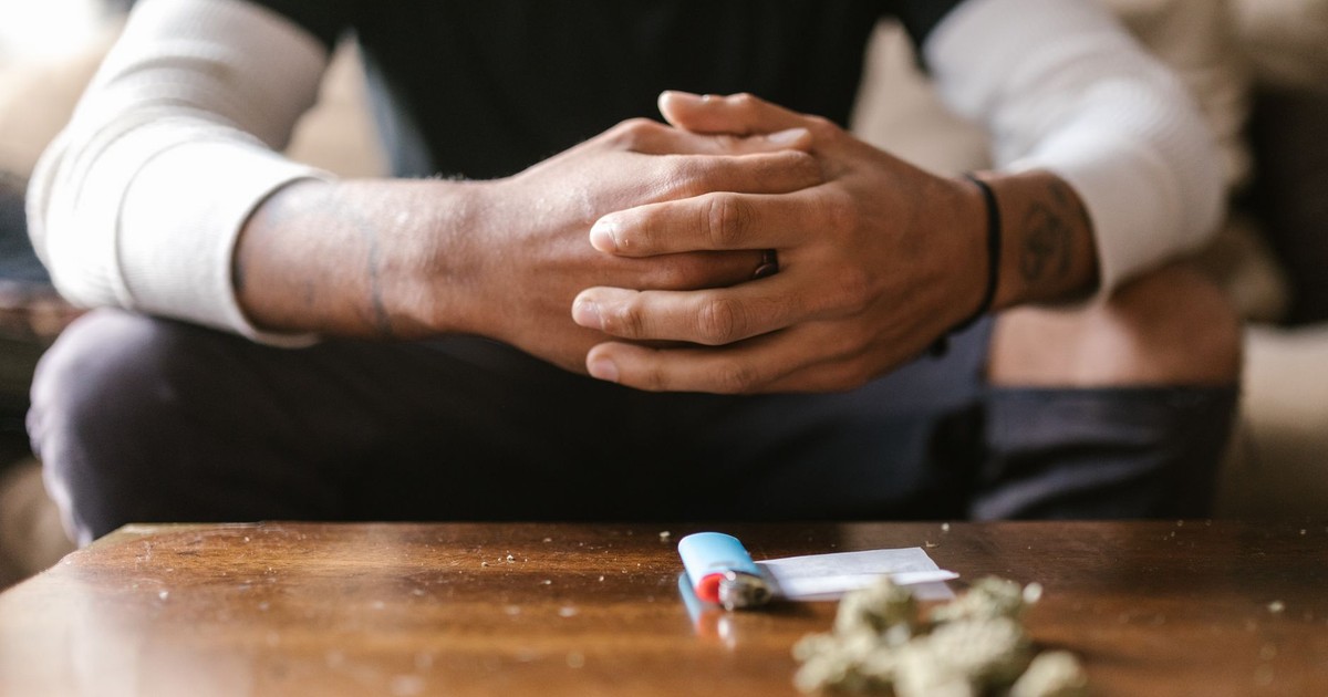 A person resting hands on table with cannabis and lighter visible in foreground.
