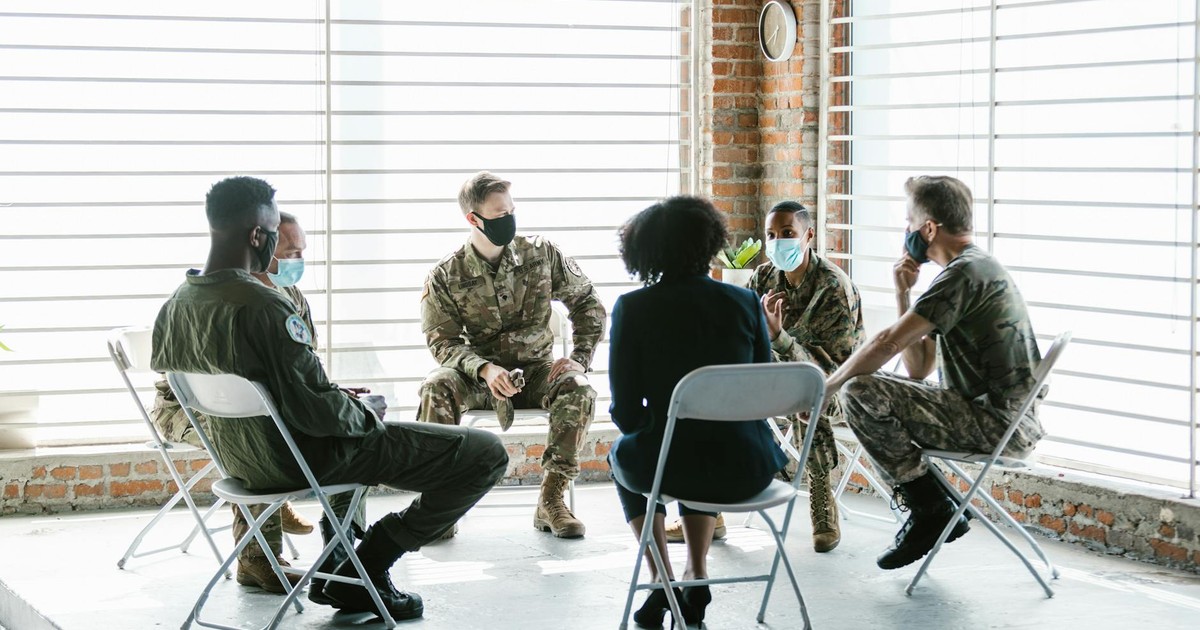 A group therapy session with soldiers in military uniform and face masks indoors.