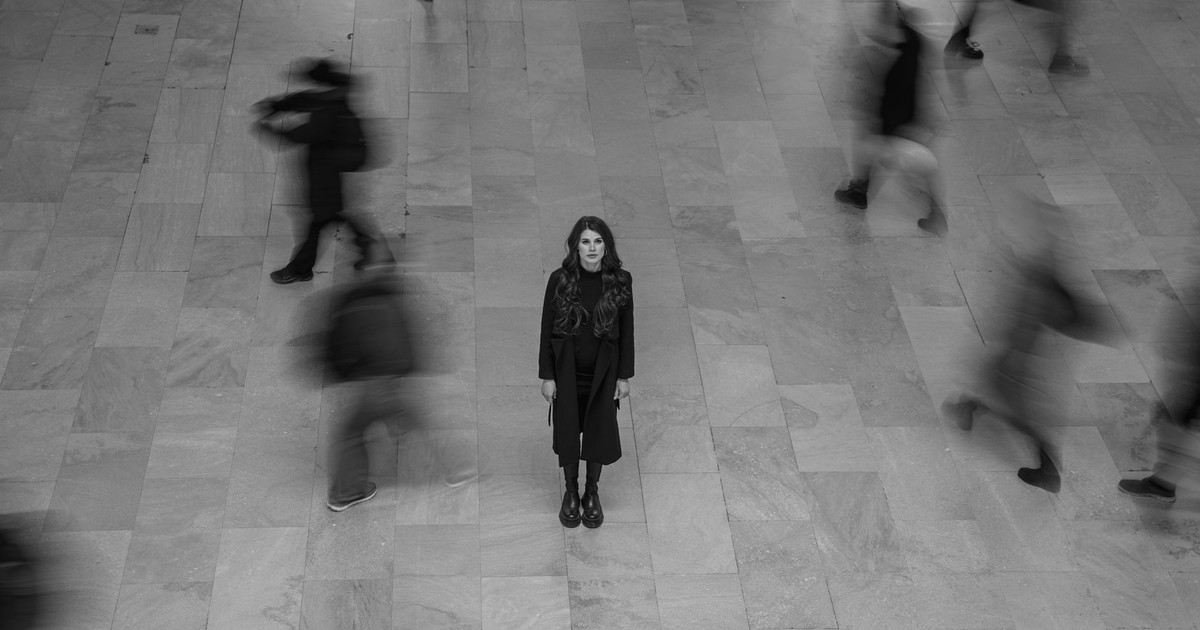 A solitary woman stands amidst blurred crowd movement in a New York terminal.