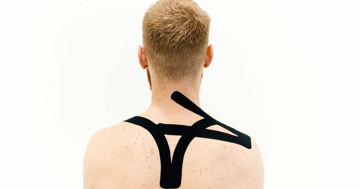 A man with kinesiology tape applied on shoulders. Back view against white background.
