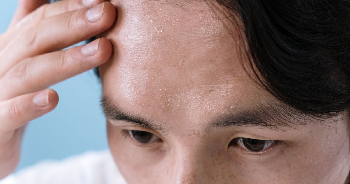 Close-up of a man with sweat on his forehead, touching it with his hand, conveying stress or illness.