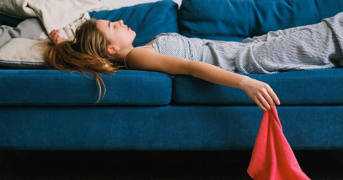 Side view of young exhausted woman with rag lying on couch in living room in daylight