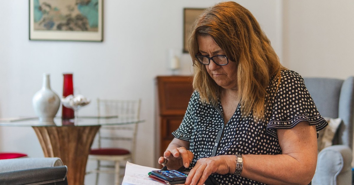 Focused woman calculating expenses with calculator and notebook at home.