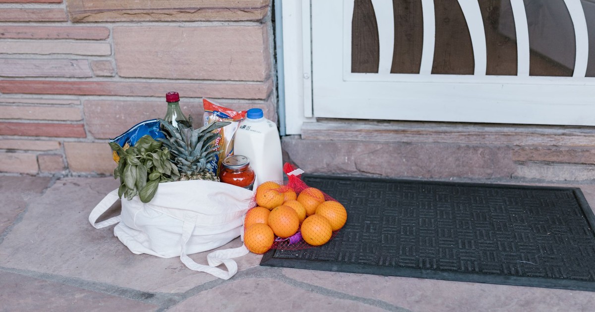 Reusable bag with groceries and fruits left at doorstep, highlighting delivery service.