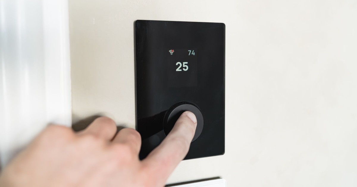 Close-up of a hand adjusting a sleek, modern smart thermostat on a wall.