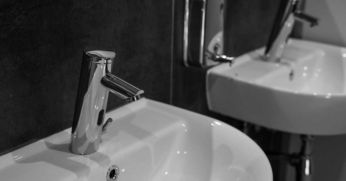 Close-up of a modern stainless steel faucet and sink in a minimalist bathroom setting.