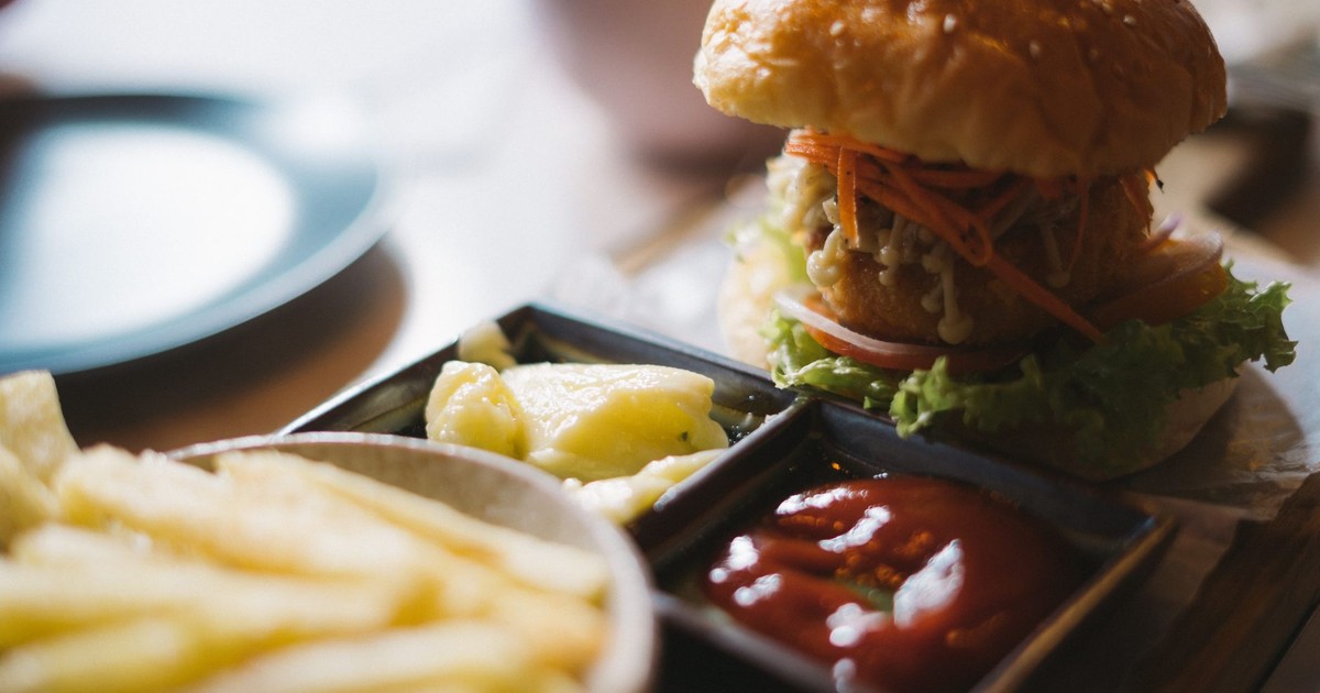 Close-up of a delicious burger with sides of fries and sauces, ideal for fast food lovers.