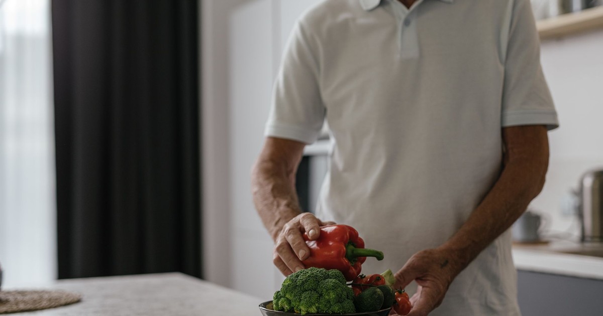 Elderly man in kitchen holding vegetables, embracing a healthy lifestyle.