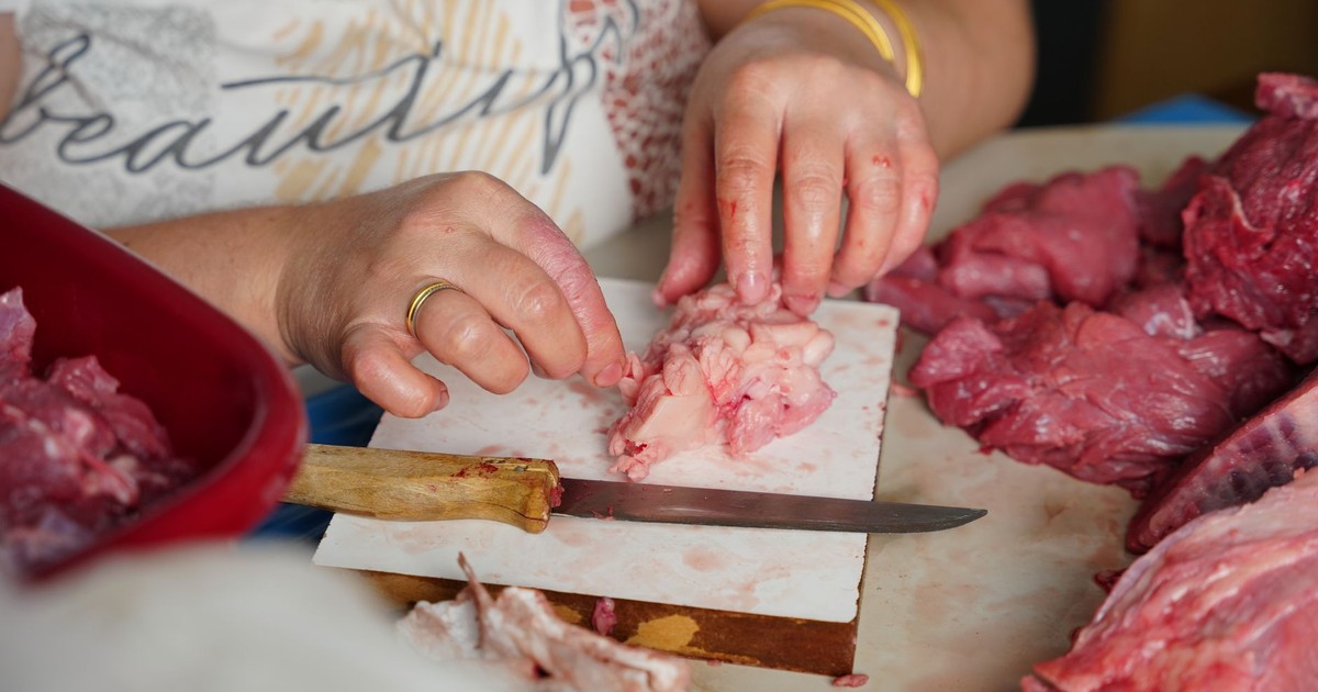 A butcher meticulously trimming fresh cuts of meat on a counter indoors with a knife.