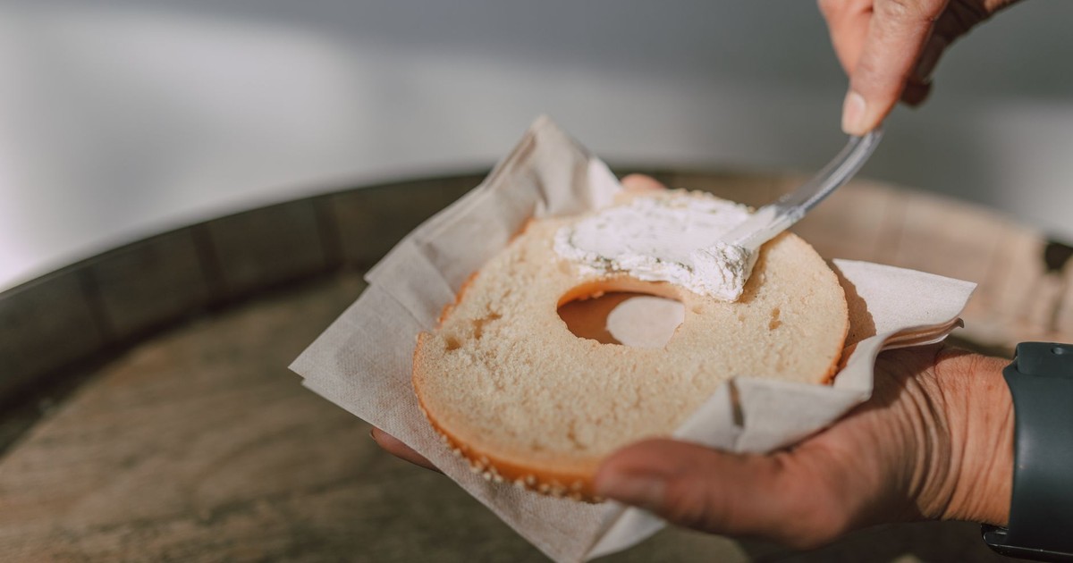 Close-up of hands spreading creamy cheese on a sliced bagel.