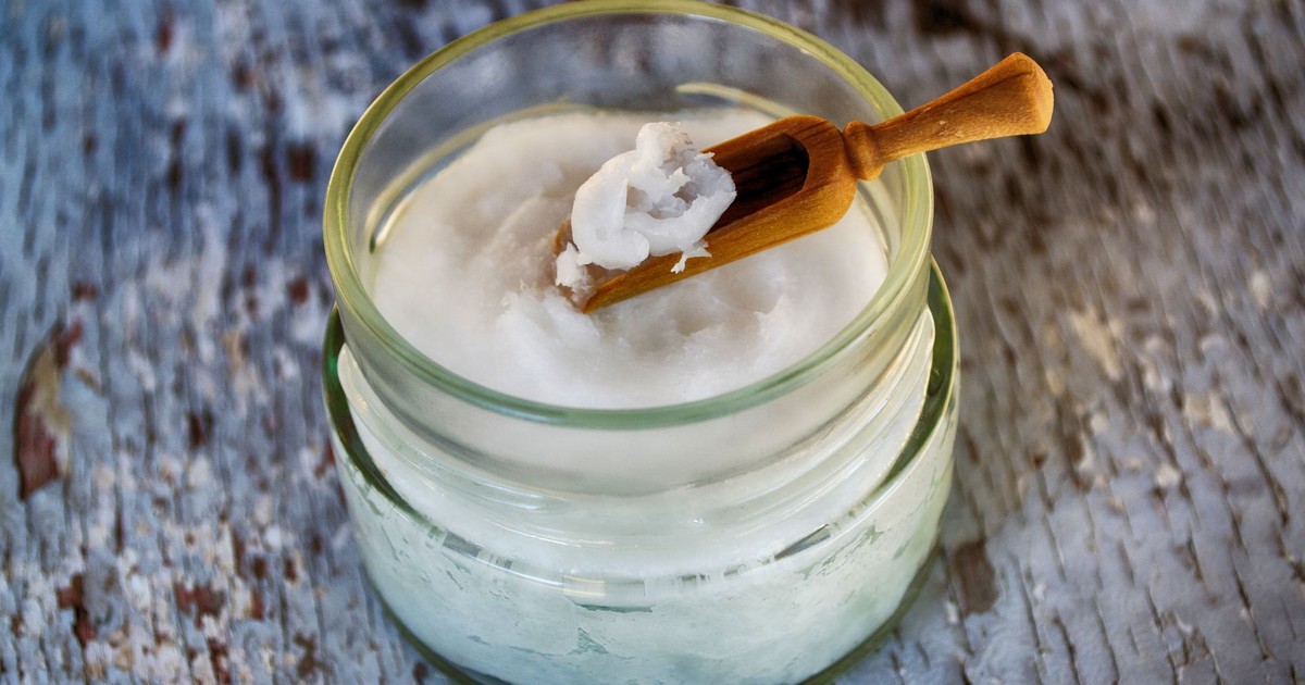 Close-up of organic coconut oil in glass jar with wooden spoon, perfect for natural health and wellness use.