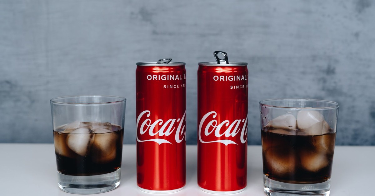 Two cans of soda with ice-filled glasses on a minimalistic background.