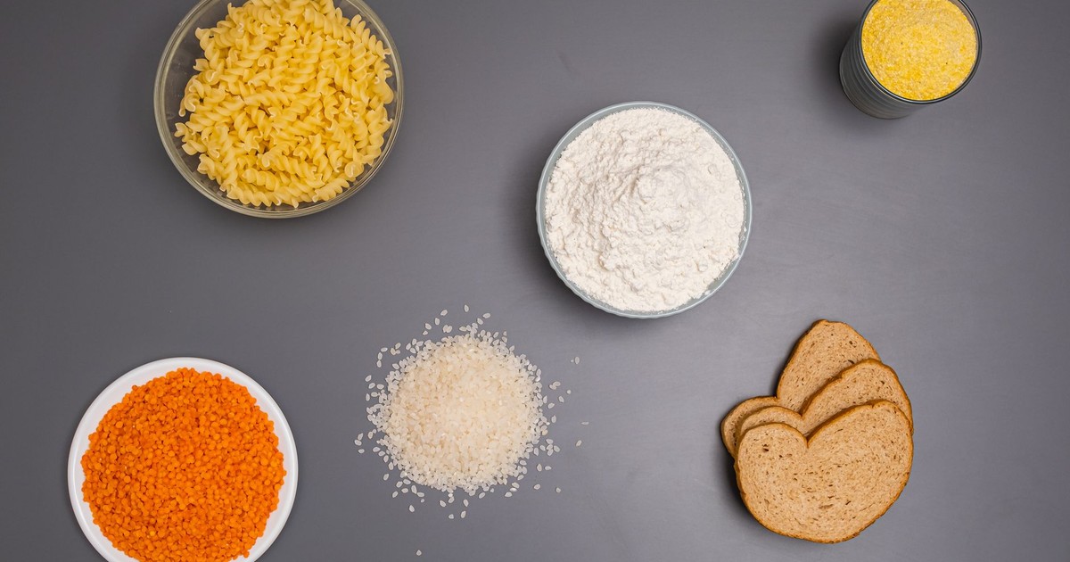 An assortment of dry ingredients including pasta, rice, and bread displayed on a grey background.