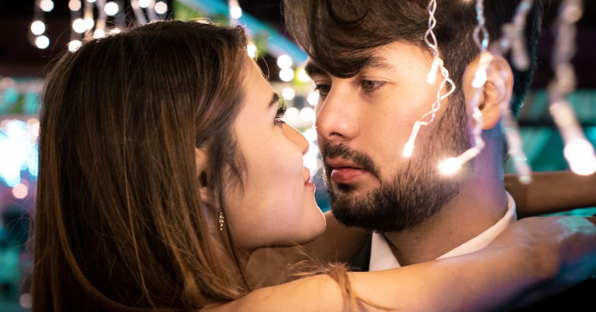 Close-up of a young couple embracing and gazing at each other romantically under string lights.