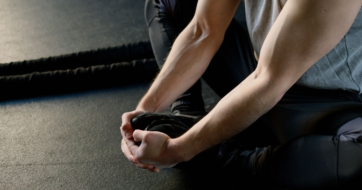 Man sitting on gym floor, stretching legs, preparing for workout routine.