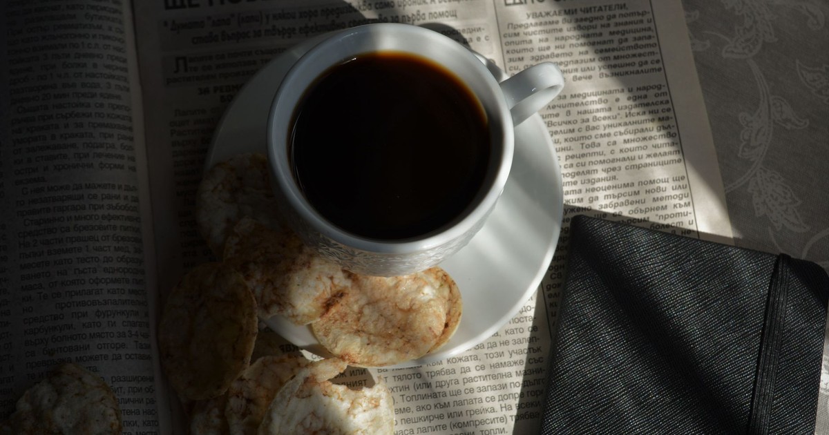 A cozy setup featuring a cup of black coffee, biscuits, and a newspaper, perfect for a relaxed morning.