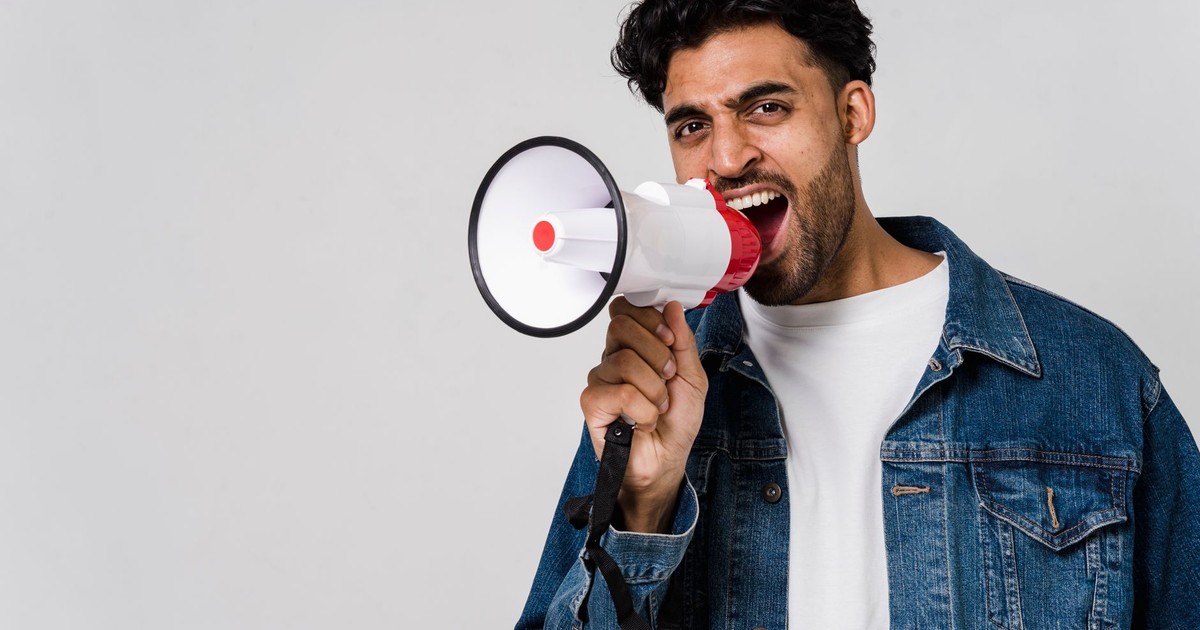 Energetic young man shouting into a megaphone, expressing enthusiasm in a studio setting.