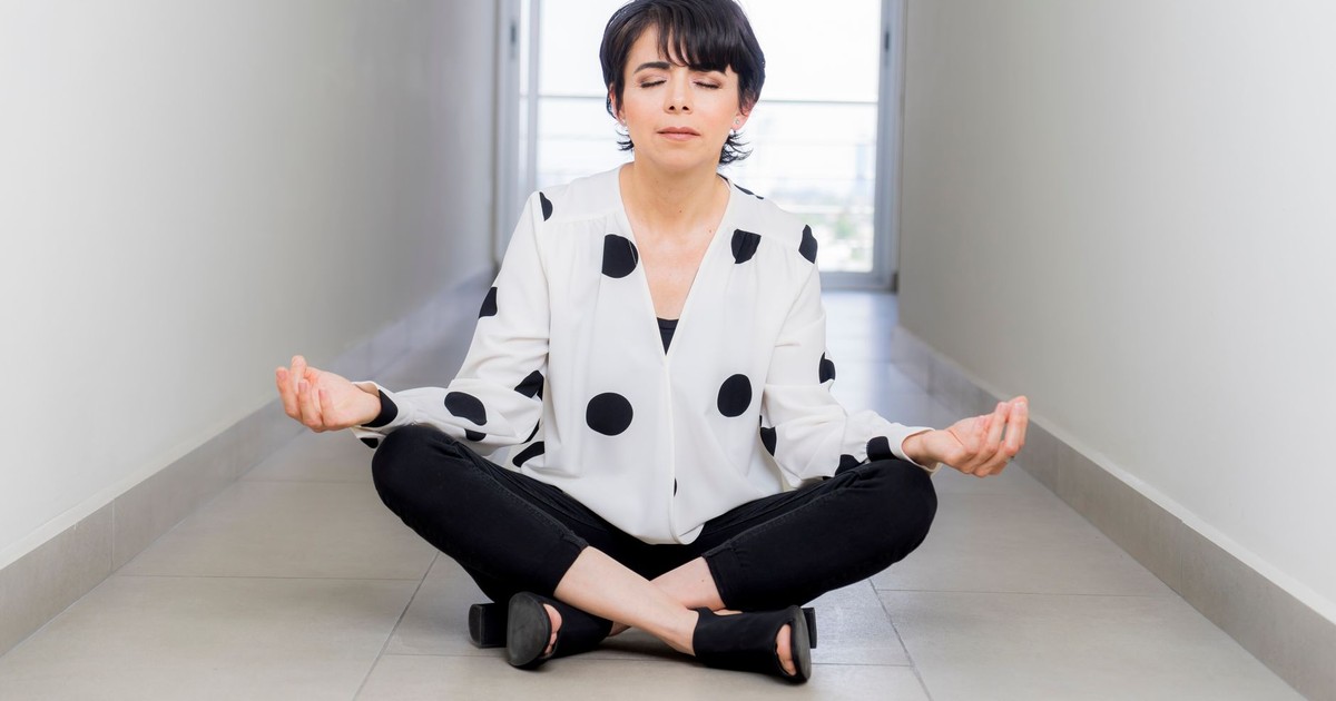 A woman practices meditation seated cross-legged in a calm and serene indoor hallway.