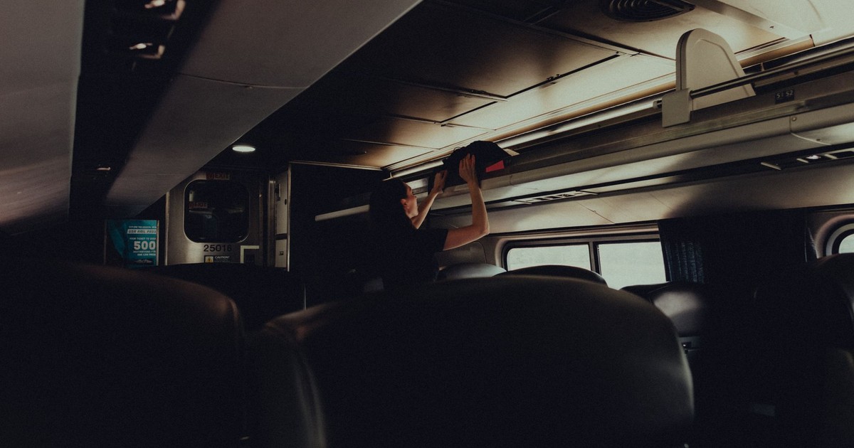 A woman placing her bag in the overhead rack on a modern train.