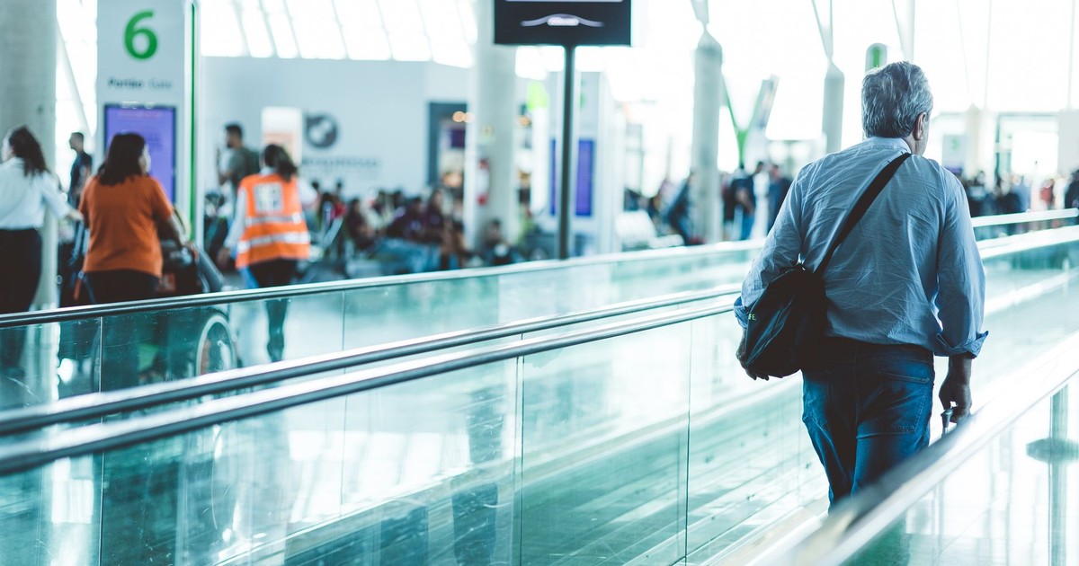 A bustling airport scene with travelers on a moving walkway in a modern terminal.