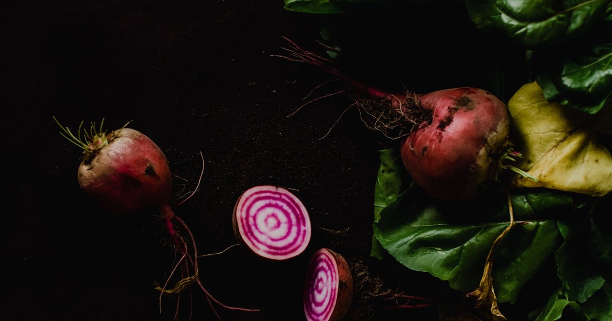 A close-up of fresh Chioggia beets with vibrant leaves on a dark background, highlighting their organic, nutritious appeal.