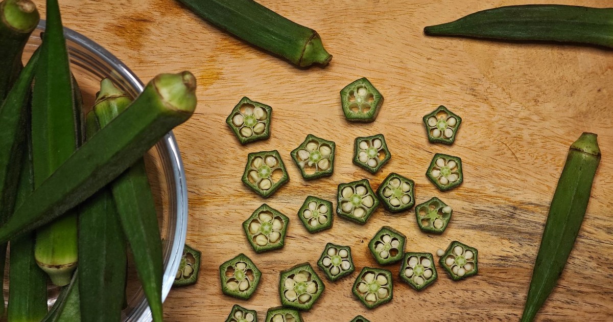 Top view of fresh and sliced okra (Abelmoschus esculentus) on a wooden surface, showcasing natural textures and colors.