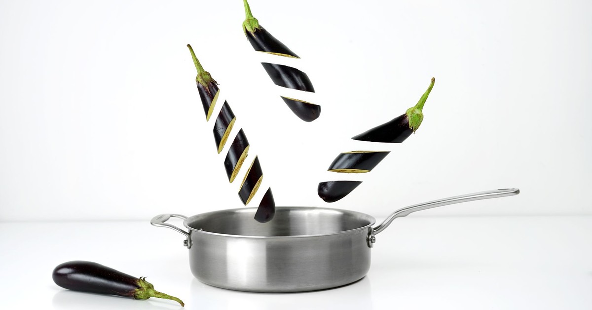 Creative image of sliced eggplants floating above a stainless steel pan against a white background.