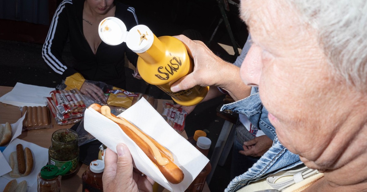 Close-up of hot dog being prepared with mustard at an outdoor party.