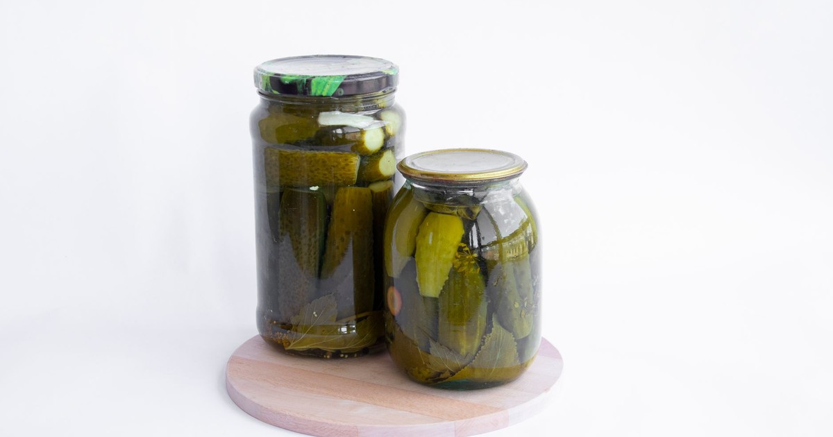 Two jars of pickles sit on a wooden board, showcasing preserved cucumbers in a still life composition.