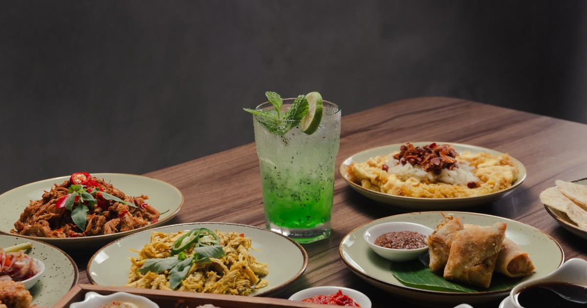 A tempting spread of Asian dishes paired with a refreshing green cocktail on a wooden table.