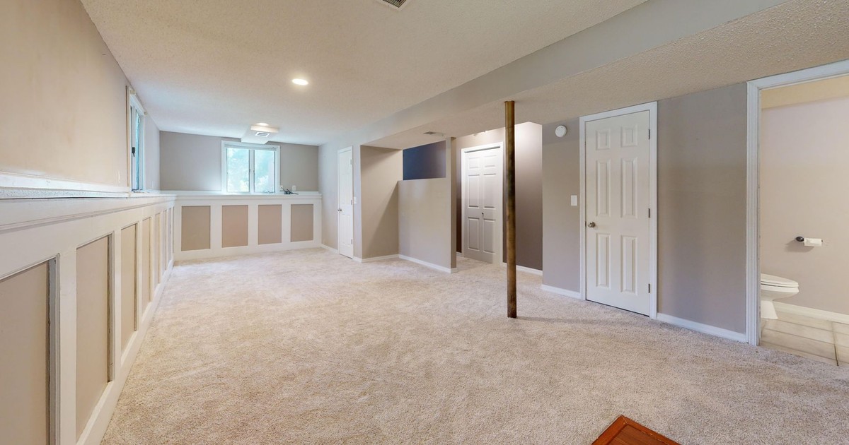 Bright and clean modern basement with carpet flooring and recessed lighting.