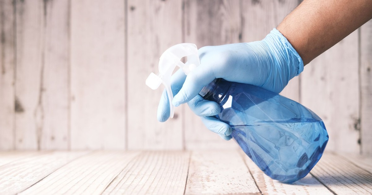 A gloved hand holding a blue spray bottle against a wooden background.