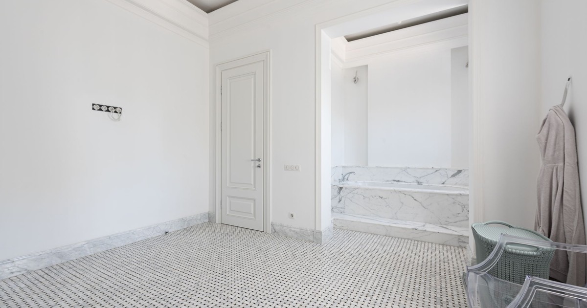 Spacious white bathroom with marble decor, featuring a bathrobe and modern chair.