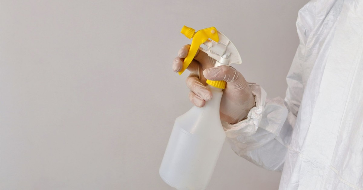 Person in protective gear holding a spray bottle inside a laboratory setting.