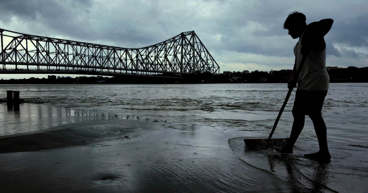 Silhouette of a worker sweeping by the Howrah Bridge during moody evening.