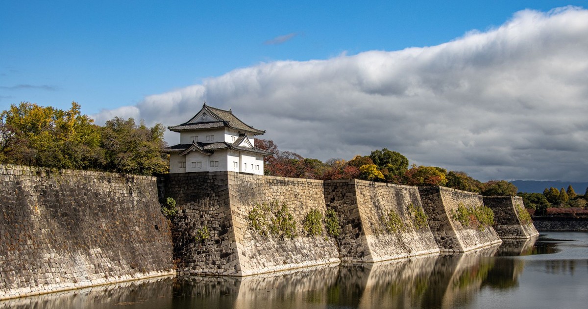 Scenic view of Osaka Castle walls reflecting on the calm moat water under a bright sky.