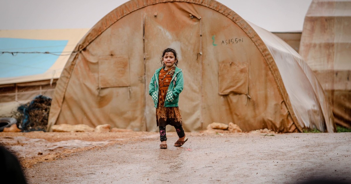 A young girl in a green jacket walks in a refugee camp in Idlib, Syria.