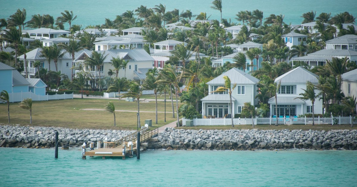 Aerial view of luxury coastal residences with palm trees by turquoise waters.