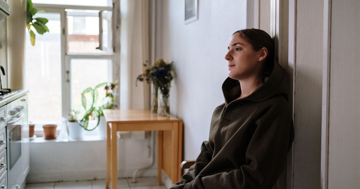 Pensive woman in a hoodie sitting indoors by a window, capturing a moment of reflection.