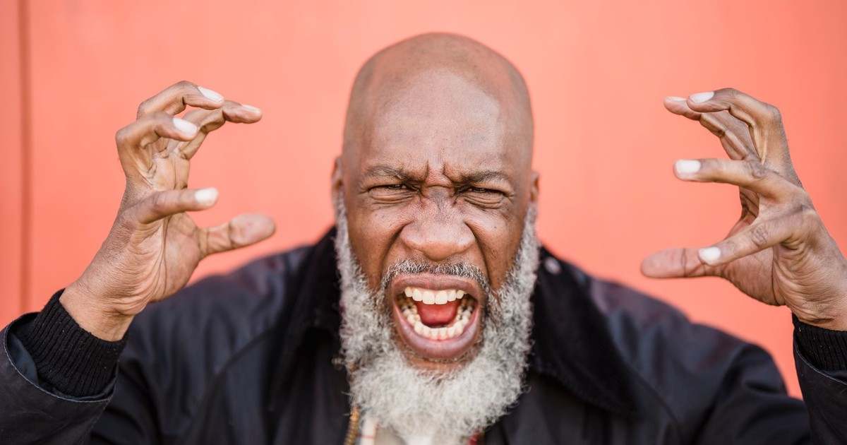 An elderly man with a beard expresses intense frustration against a striking orange background.