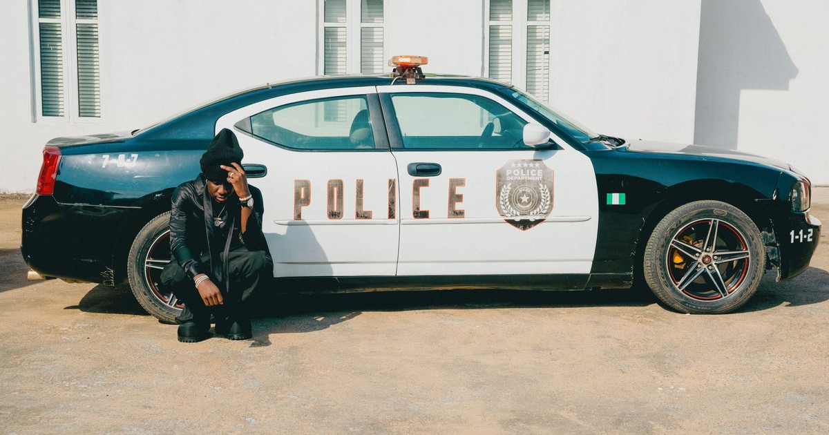 Police officer seated by car in urban area during the day.