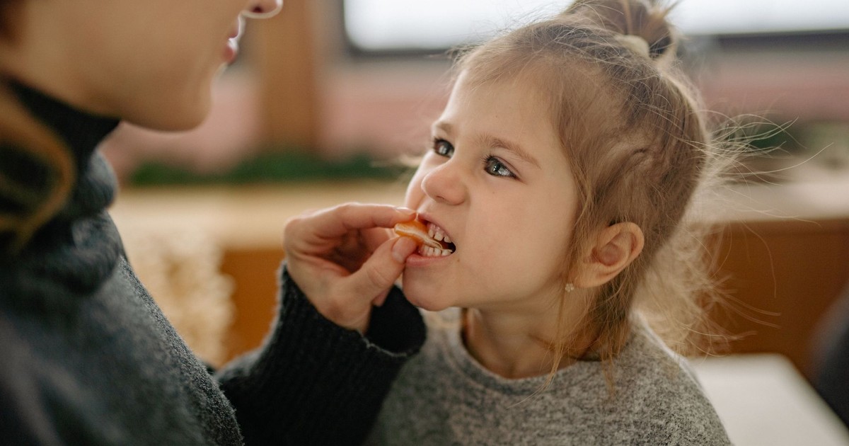 A parent feeding a young girl a piece of fruit in a cozy home setting.