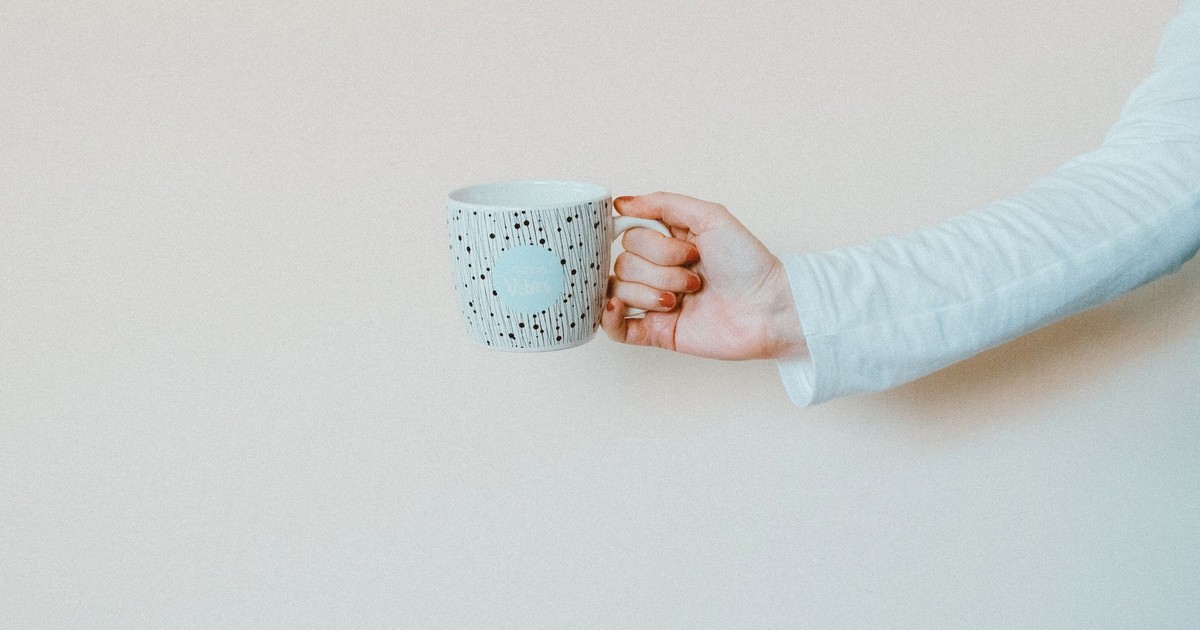 A hand holding a patterned coffee mug against a minimalist background, perfect for lifestyle themes.